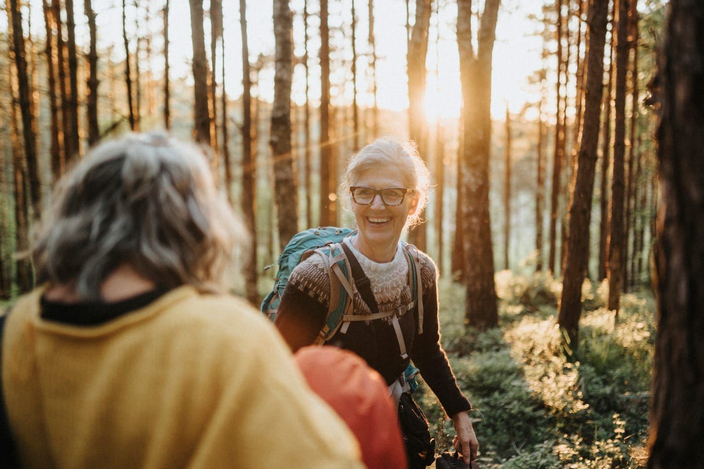 Two older women hiking and laughing in a pine forest
